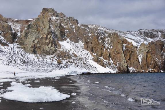 A praia termina nas escarpas rochosas que formavam a parede da caldeira vulcânica que hoje é Deception Island, na Antártida